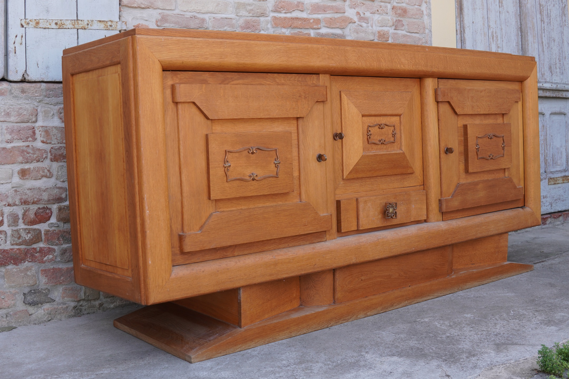 Art Deco Sideboard by Gaston Poisson – A Masterpiece of French Oak Craftsmanship An exceptional example of French Art Deco design, this remarkable sideboard attributed to Gaston Poisson embodies the refined balance between architectural rigour and artisanal sophistication that defined the finest furniture of the interwar period. Expertly handcrafted in solid oak, the piece showcases a striking interplay of geometric volumes, stepped detailing and sculptural proportions, all softened by the warmth and expressive grain of the timber. The façade is distinguished by its elegantly panelled doors, enriched with subtle carved embellishments and original decorative hardware, reflecting Poisson's celebrated ability to merge traditional cabinet-making techniques with the modern spirit of the 1920s and 1930s. Resting upon a substantial plinth base, the sideboard possesses a commanding presence while maintaining an understated elegance suitable for both classic and contemporary interiors. Beyond its visual appeal, this is a work of outstanding functionality, offering generous storage concealed behind beautifully executed cabinetry. A testament to the enduring quality of French craftsmanship, it represents not merely a piece of furniture but a highly decorative object of historical significance. A rare acquisition for discerning collectors and connoisseurs of twentieth-century design, this Art Deco sideboard exemplifies the timeless sophistication associated with the finest creations of Gaston Poisson. #GastonPoisson #FrenchArtDeco #SolidOakFurniture #ArtDecoInteriors #CollectorsDesign