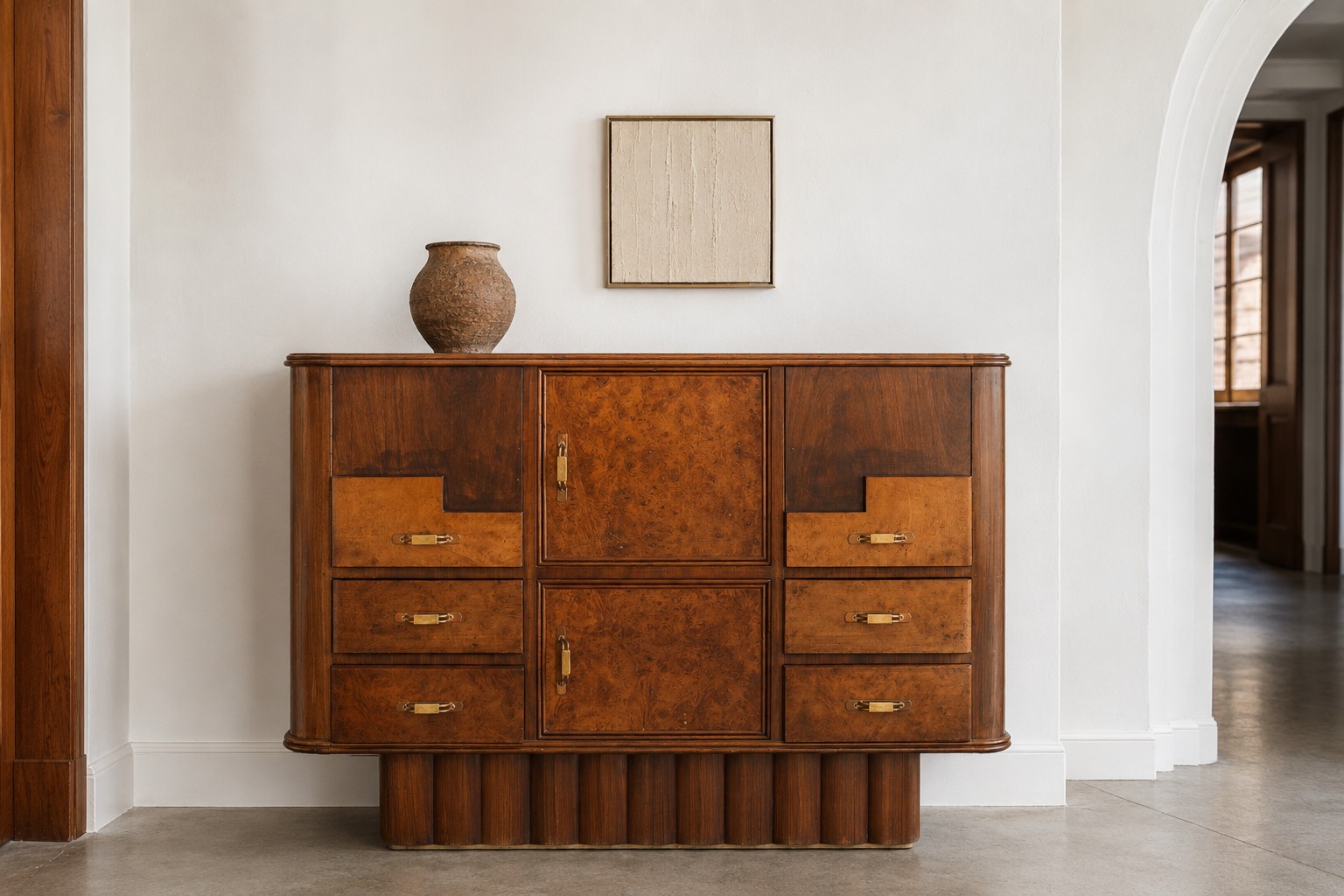 xceptional Italian Art Deco Bar Cabinet, circa 1925 An exceptional and highly unusual Italian cabinet dating from the mid-1920s, masterfully crafted in richly figured walnut and burr walnut. Conceived with remarkable ingenuity, the piece conceals a beautifully appointed drop-front cocktail compartment, transforming from an imposing sideboard into an elegant home bar with effortless sophistication. The architectural façade is characterised by a harmonious arrangement of drawers and cupboards framed by softly rounded corners, while the stepped geometry and powerful fluted plinth reveal early Rationalist sensibilities with an almost proto-Brutalist presence. Original Bakelite and brass handles provide refined period detailing, perfectly complementing the warmth and depth of the veneers. The central panel ingeniously folds down to reveal a fitted bar compartment, embodying the luxurious and practical spirit of the finest Italian furniture of the interwar years. Such transformable pieces were intended for grand residences and fashionable salons, combining functionality with a distinctly modern vision. Executed with exceptional craftsmanship, the cabinet retains a magnificent mellow patina and displays the restrained elegance associated with the finest Italian decorative arts between the wars. The monumental base and architectural proportions anticipate the language that would later define Italian Rationalism, making this an extraordinarily decorative and collectible statement piece. Origin: Italy Period: Circa 1925 Style: Art Deco with early Rationalist and proto-Brutalist influences Materials: Walnut, burr walnut, original Bakelite and brass handles Features: Concealed drop-front cocktail compartment transforming into a bar cabinet Condition: Very good vintage condition, with an attractive age-related patina and minor wear consistent with careful use. #ItalianArtDeco #RationalistDesign #BurrWalnutFurniture #VintageBarCabinet #CollectorsInterior