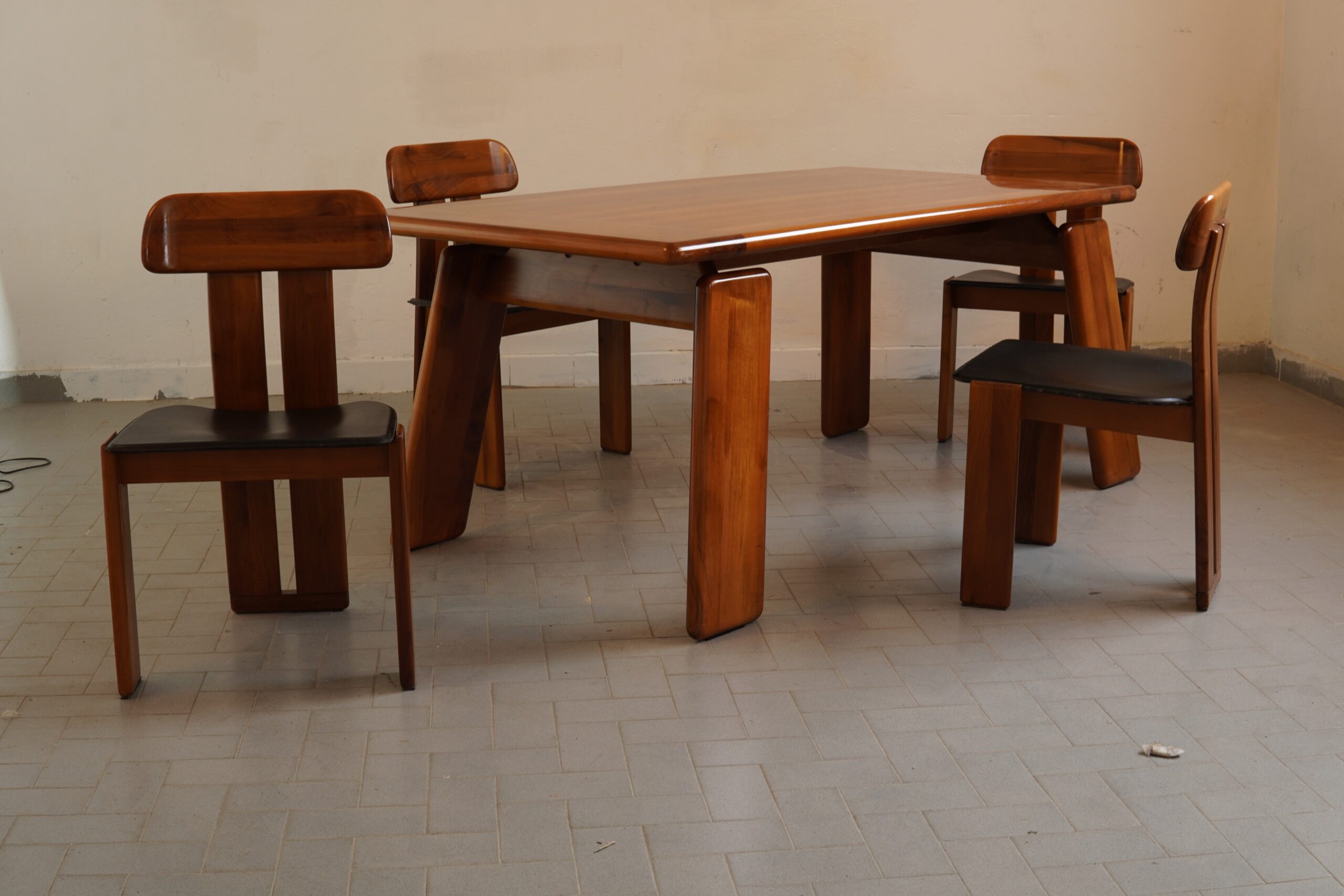 An exceptional **“Sapporo” dining suite**, designed by **Mario Marenco** for **Mobil Girgi**, Italy, circa 1970. Comprising a substantial dining table and four matching chairs, the suite is distinguished by its sculptural timber construction, beautifully rounded profiles and original black leather seats. The architectural legs and gently curved chair backs lend the ensemble an almost monumental presence, whilst retaining the warmth and refinement associated with the finest Italian cabinetmaking of the period. The timber displays a particularly rich colour and a most attractive, naturally developed patina. A remarkably handsome and increasingly sought-after example of 1970s Italian design. **Mario Marenco (1933–2019)** was an Italian architect, industrial designer, actor and celebrated wit. After graduating in architecture from the University of Naples, he continued his research in Stockholm and Chicago before establishing his own practice in Rome. He designed for several of Italy’s most distinguished manufacturers, including Arflex, Artemide, Bernini and Mobil Girgi. His work is admired for its bold proportions, architectural clarity and unmistakably playful intelligence. #MarioMarenco #MobilGirgi #SapporoDiningSet #ItalianDesign #VintageFurniture