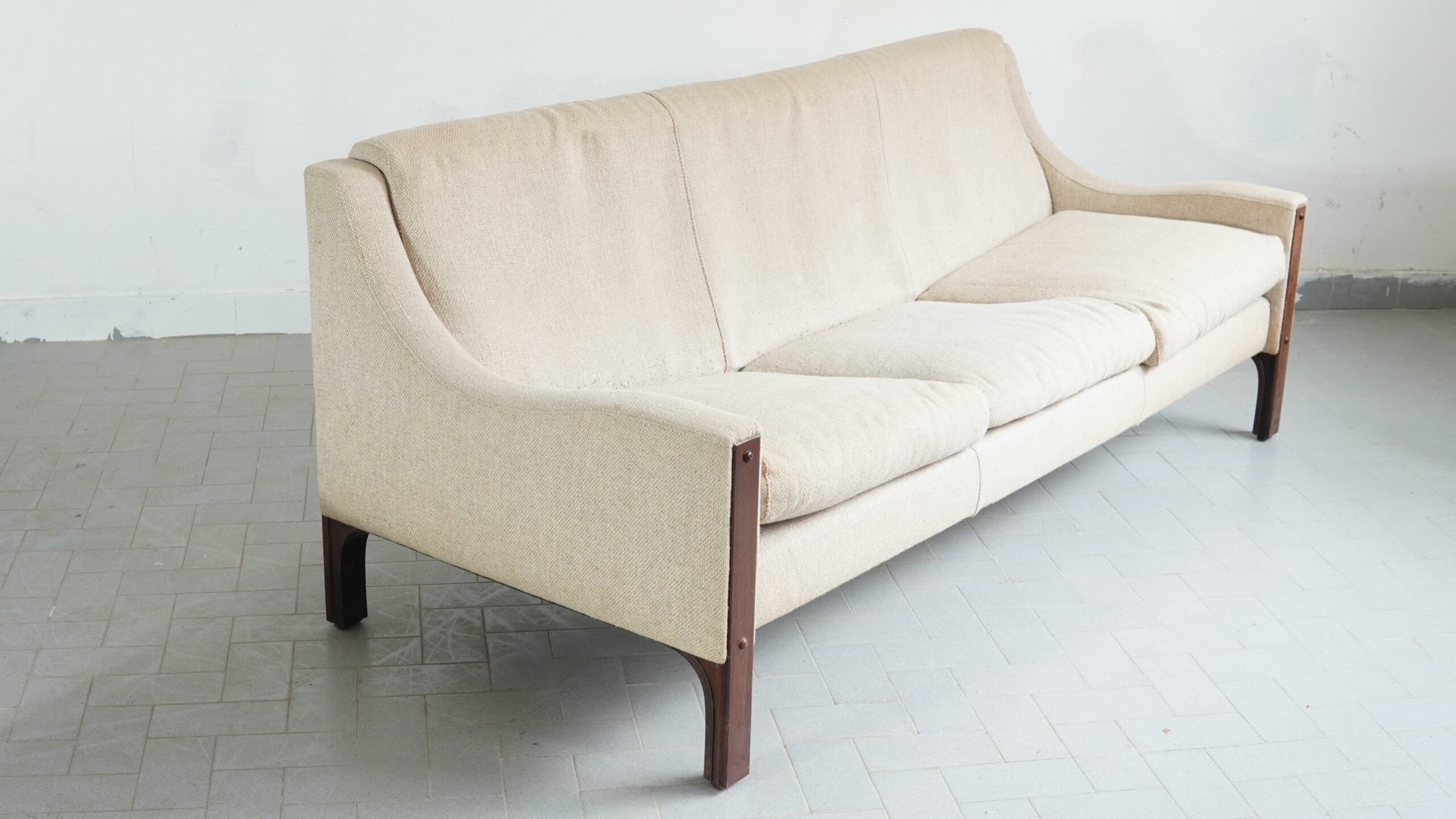 A Rare 'Wave' Sofa by Tito Agnoli for Mobilia, 1961 One is presented with a scarce and exceptionally refined lounge sofa, designed by Tito Agnoli and manufactured by Mobilia in 1961. Its structure is executed in rosewood, the dark timber offering a striking contrast to the current white bouclé upholstery—a juxtaposition of materials that speaks to Agnoli’s singular sensibility . The sofa’s defining feature is its fluid, wave-like profile. The armrests curve with a soft, organic quality, and the upholstery on both the seat and back is divided into three distinct segments by two linings . Yet the most architecturally intriguing element remains the legs: they run the full height of the front and back, featuring a subtle double-edge detail at the base and a slight, deliberate bend at the rear—a clever play of perspective that rewards close inspection . This piece was produced in very limited quantities and is documented in G. Gramigna’s Repertorio del design italiano 1950-1980 . It represents a rare opportunity for the discerning collector to acquire a genuinely scarce work by a designer whose pieces are held in the permanent collection of the Museum of Modern Art, New York . #TitoAgnoli #Mobilia #ItalianDesign #MidCenturyModern #QuietLuxury